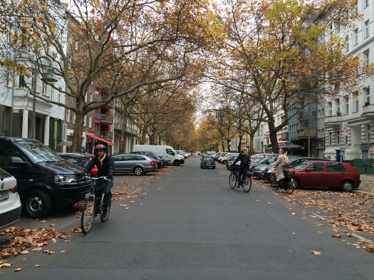 Narrow street with a strong sense of enclosure lets cyclists mix with the slow-moving cars. Small wheels are always allowed on the sidewalk.
